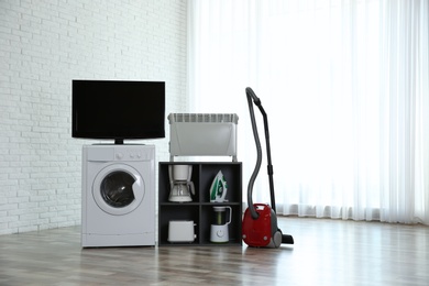 Photo of Modern vacuum cleaner and different household appliances near window indoors