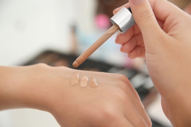Photo of Woman testing different shades of liquid foundation on her hand against blurred background, closeup