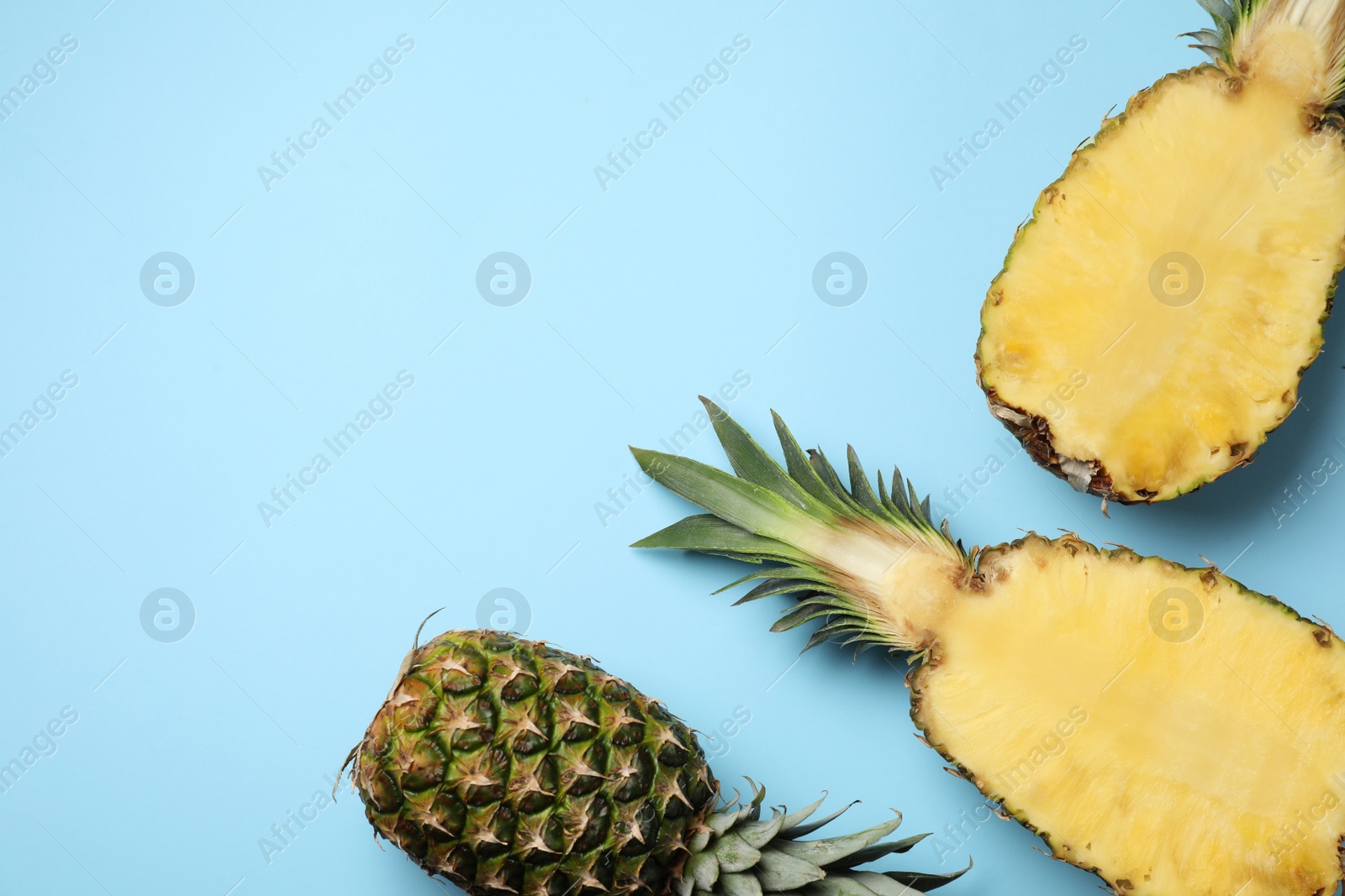 Photo of Fresh whole and cut pineapples on light blue background, top view. Space for text