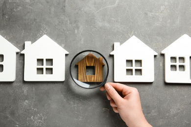 Photo of Woman with magnifying glass exploring different house models on grey stone background, top view. Search concept