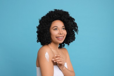 Photo of Young woman applying body cream onto shoulder on light blue background