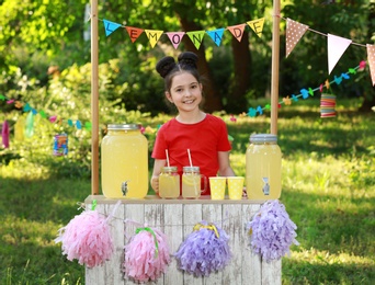 Photo of Cute little girl at lemonade stand in park. Summer refreshing natural drink