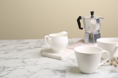 Photo of Cups, moka pot and jug on white marble table. Space for text