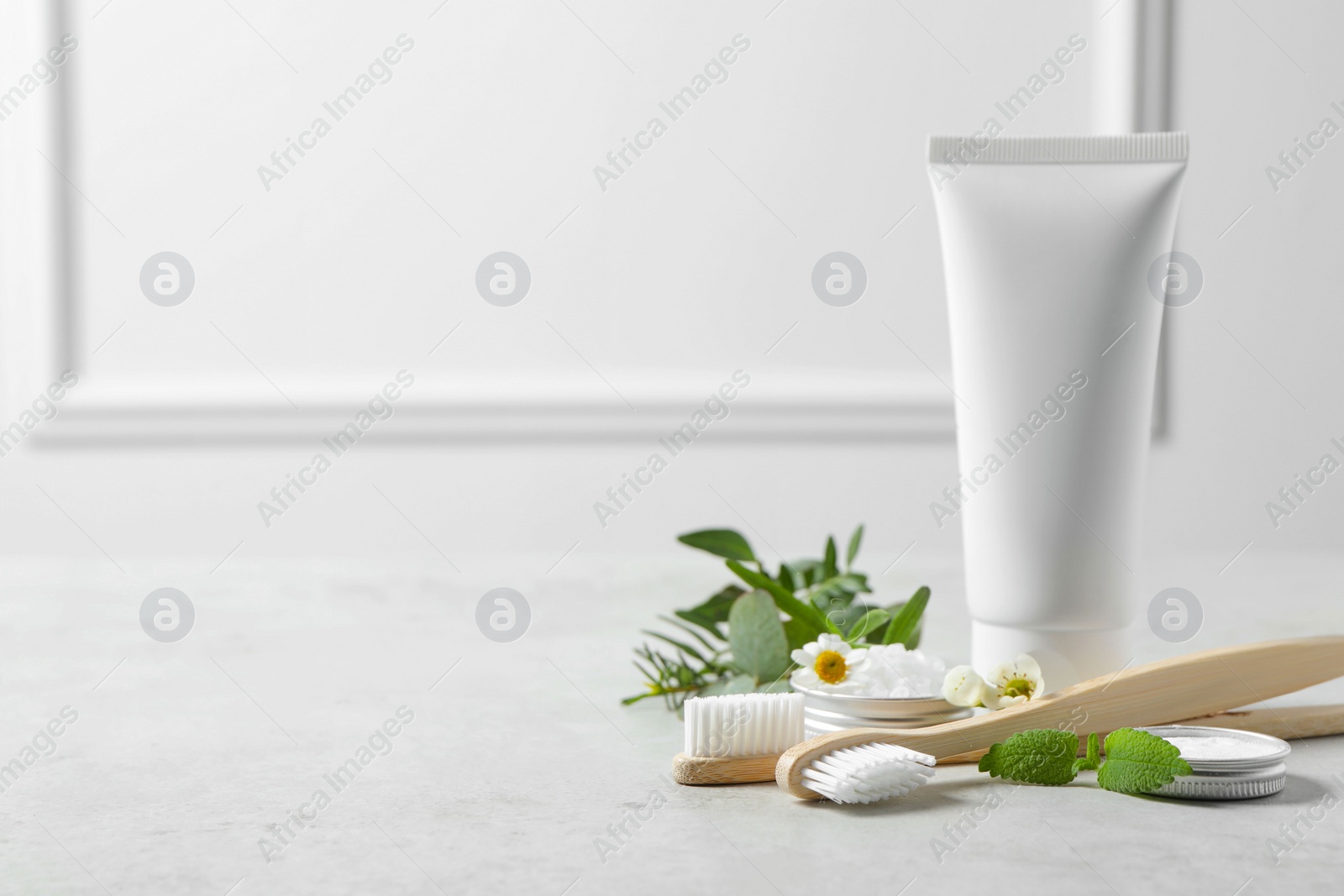 Photo of Bamboo toothbrushes, tube of cream and herbs on light grey table. Space for text