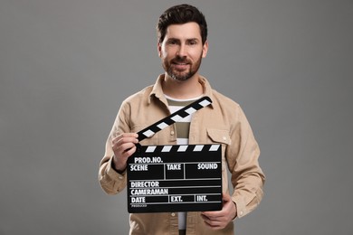 Photo of Smiling actor holding clapperboard on grey background