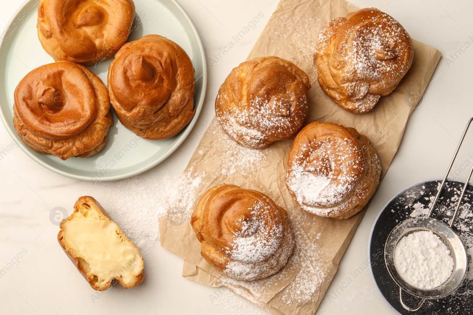 Photo of Delicious profiteroles with powdered sugar on white table, flat lay