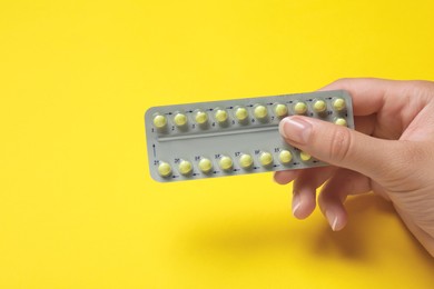 Photo of Woman holding birth control pills on yellow background, closeup