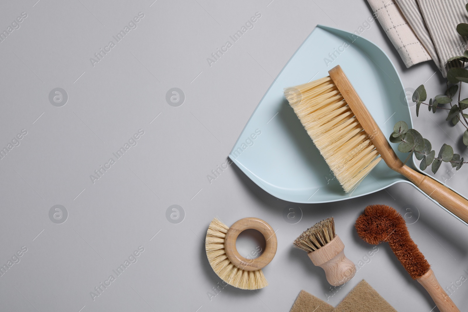 Photo of Cleaning brushes, scoop, towel and eucalyptus leaves on grey background, flat lay. Space for text