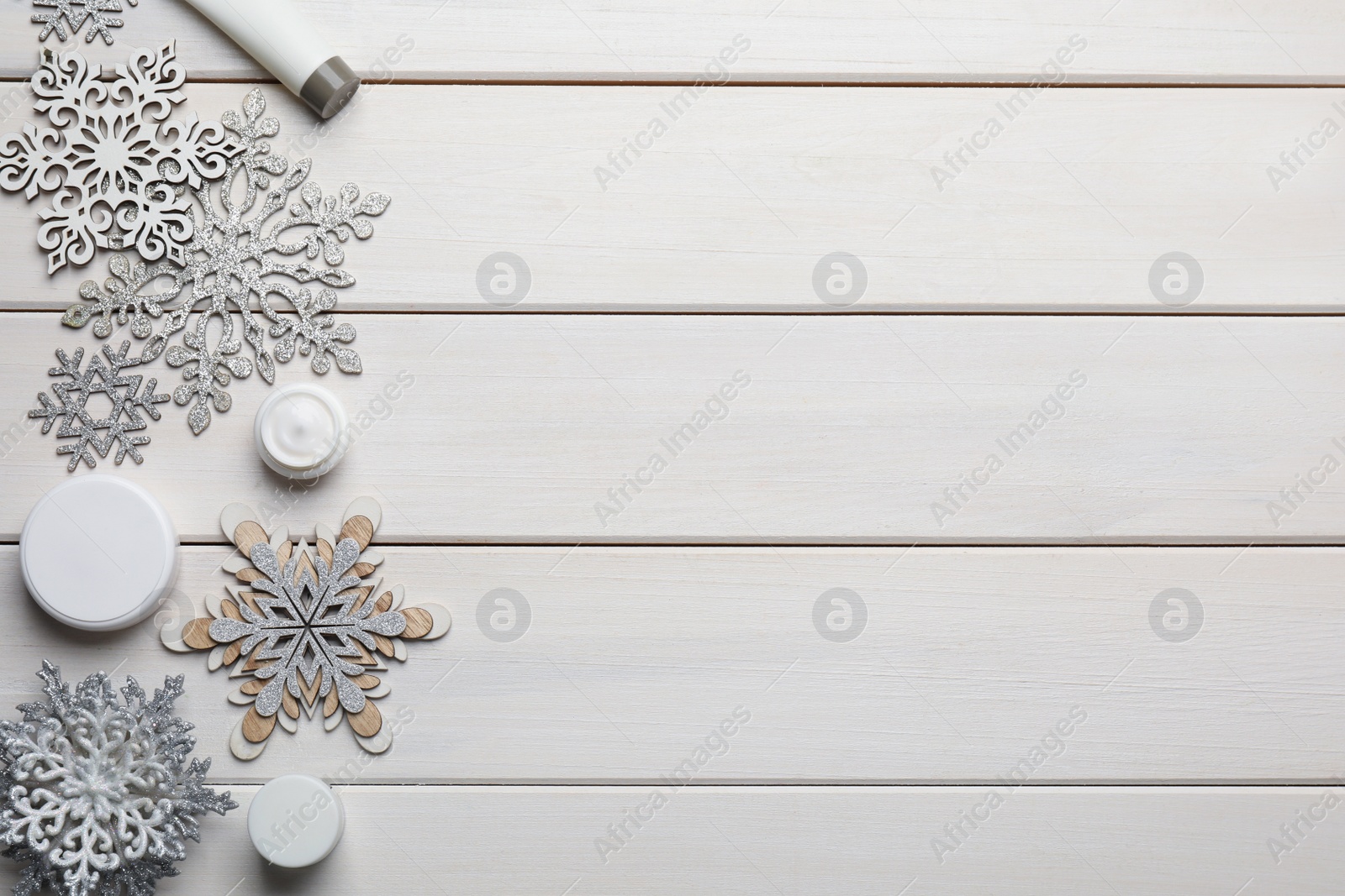 Photo of Flat lay composition with cosmetic products and snowflakes on white wooden table, space for text. Winter skin care