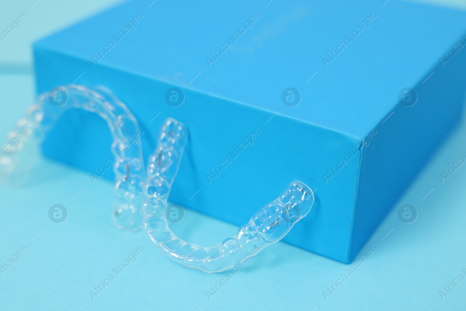 Photo of Transparent dental aligners on light blue background, closeup