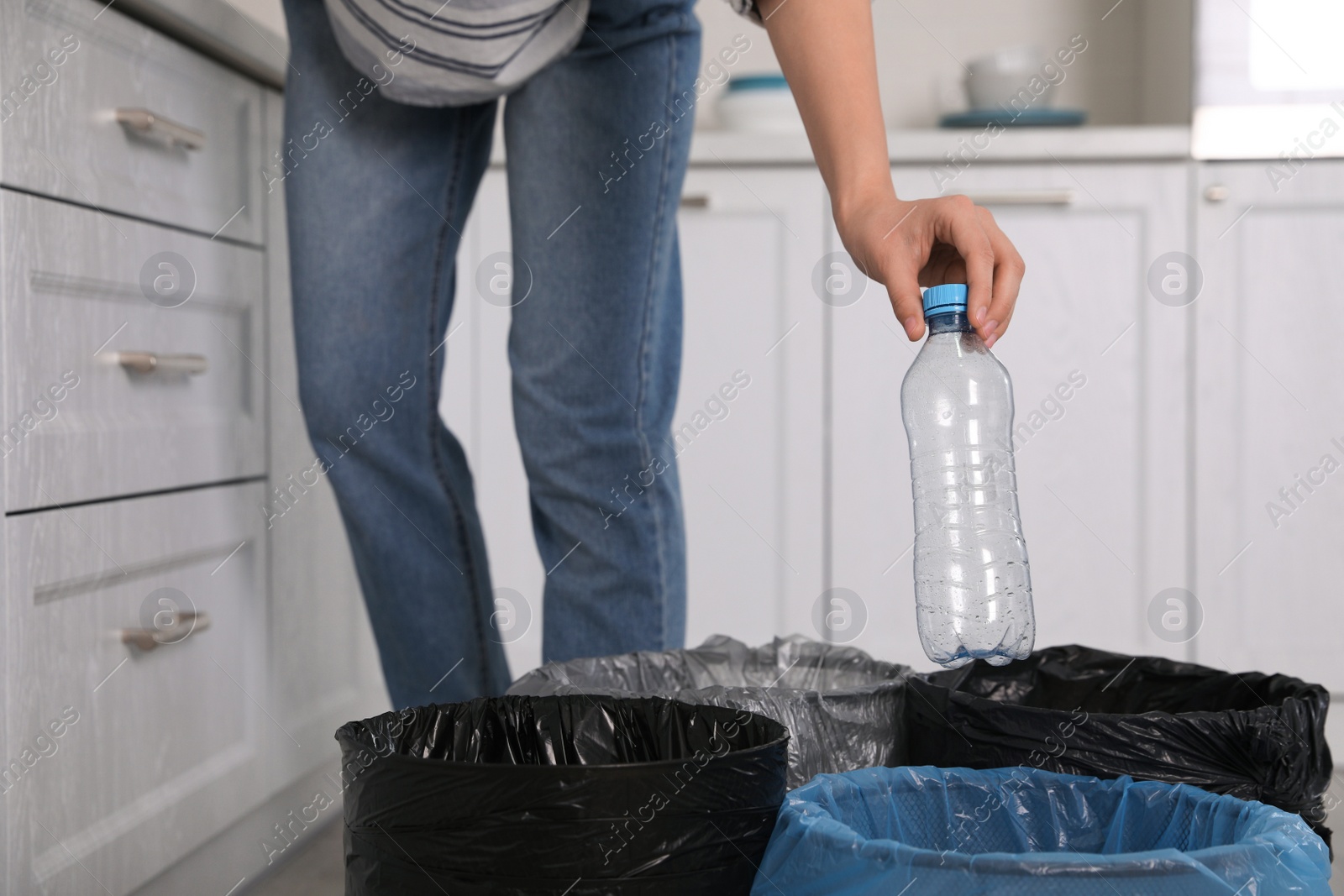 Photo of Woman throwing plastic bottle into trash bin in kitchen, closeup. Separate waste collection