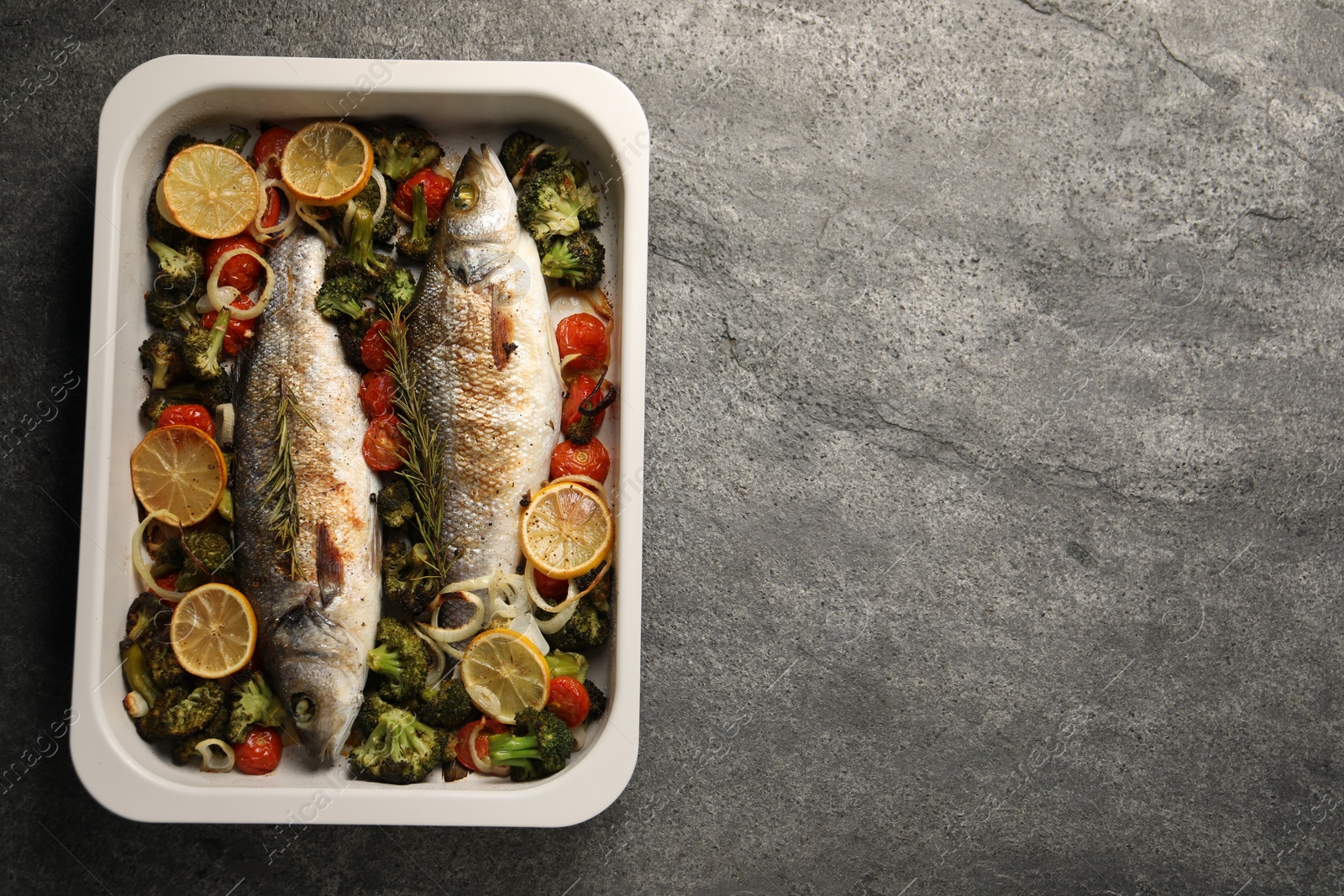 Photo of Delicious fish with vegetables and lemon in baking dish on grey textured table, top view. Space for text