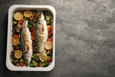 Delicious fish with vegetables and lemon in baking dish on grey textured table, top view. Space for text