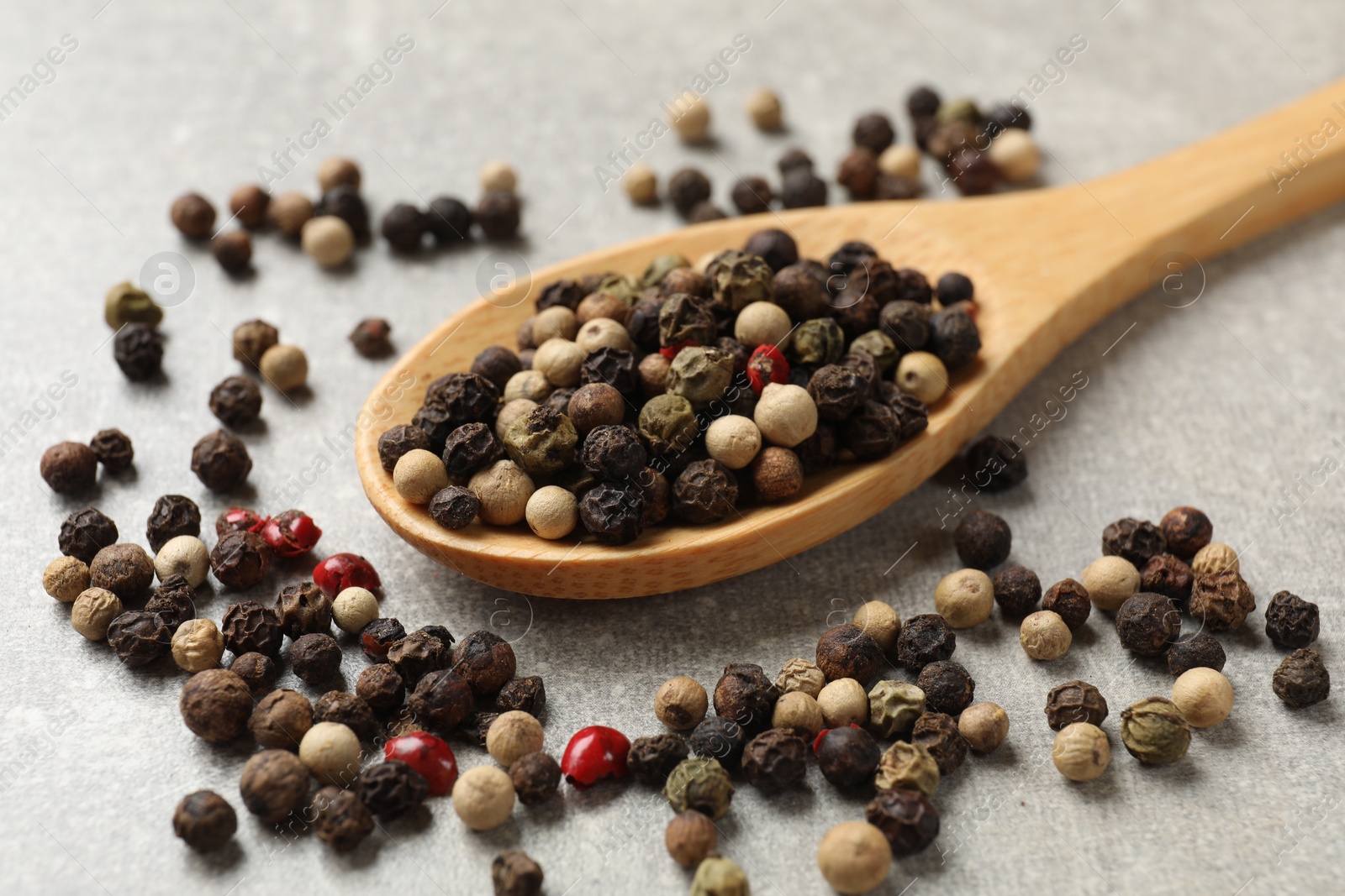 Photo of Aromatic spice. Different peppers in spoon on grey table, closeup