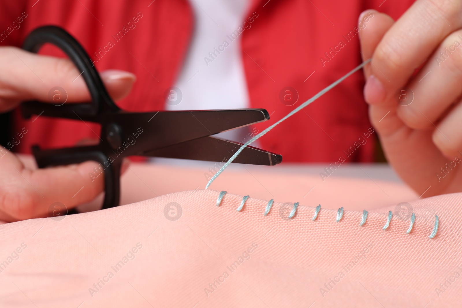 Photo of Woman cutting sewing thread over cloth, closeup