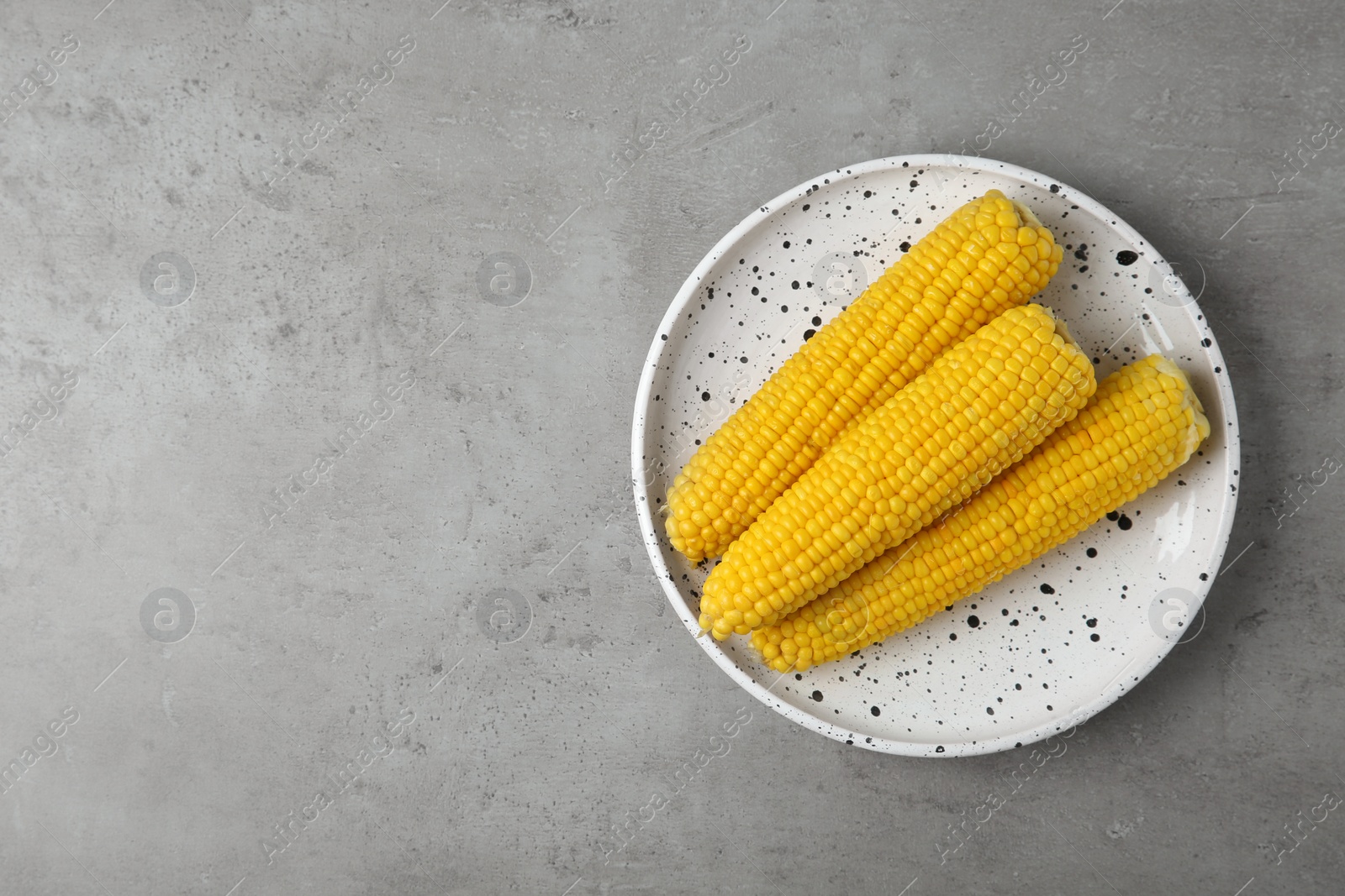 Photo of Plate with tasty boiled corn cobs on light grey table, top view. Space for text