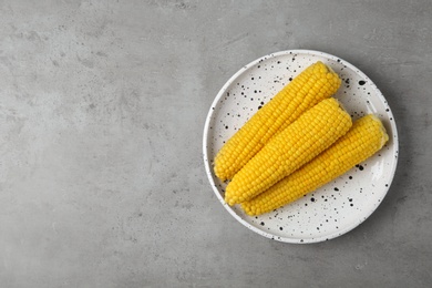 Photo of Plate with tasty boiled corn cobs on light grey table, top view. Space for text