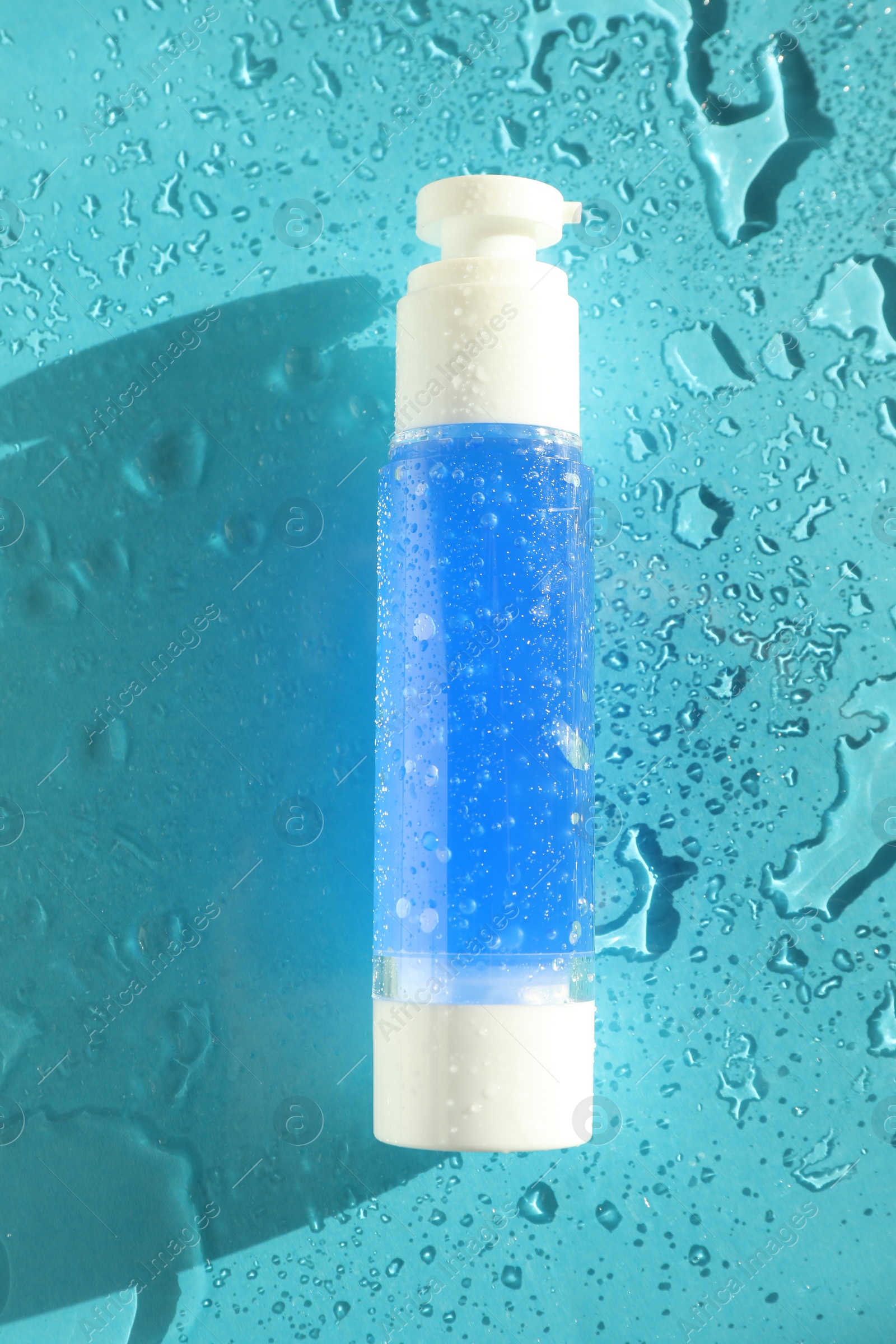 Photo of Bottle of cosmetic product on wet turquoise background, top view