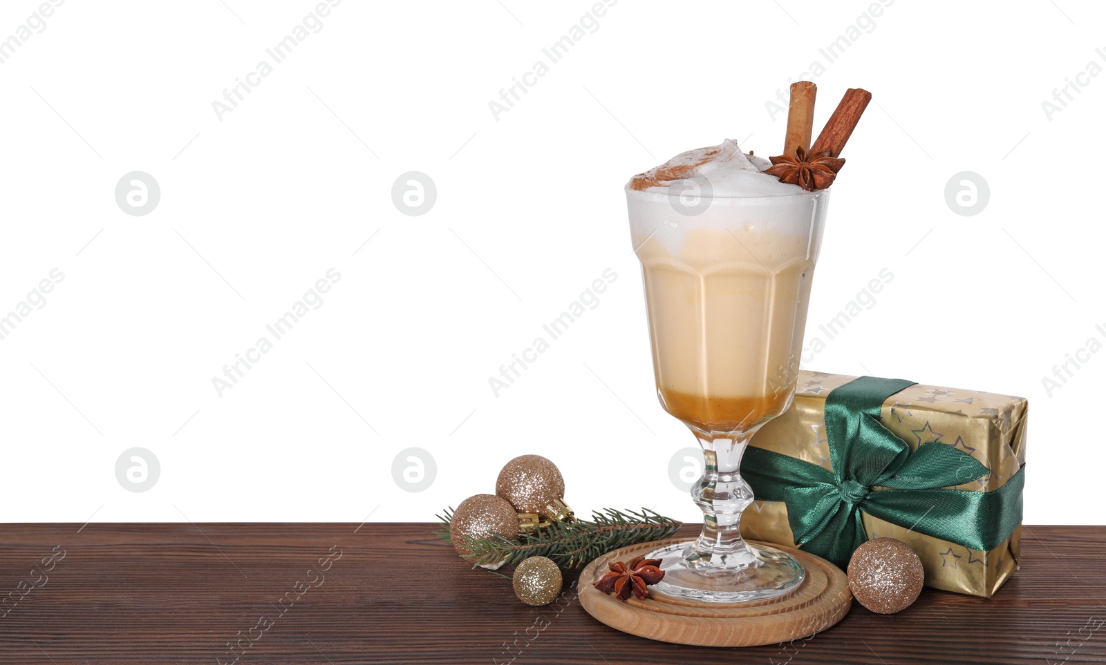 Photo of Delicious eggnog in glass, gift box and Christmas decor on wooden table against white background, space for text