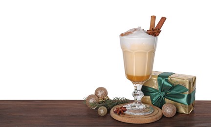 Photo of Delicious eggnog in glass, gift box and Christmas decor on wooden table against white background, space for text