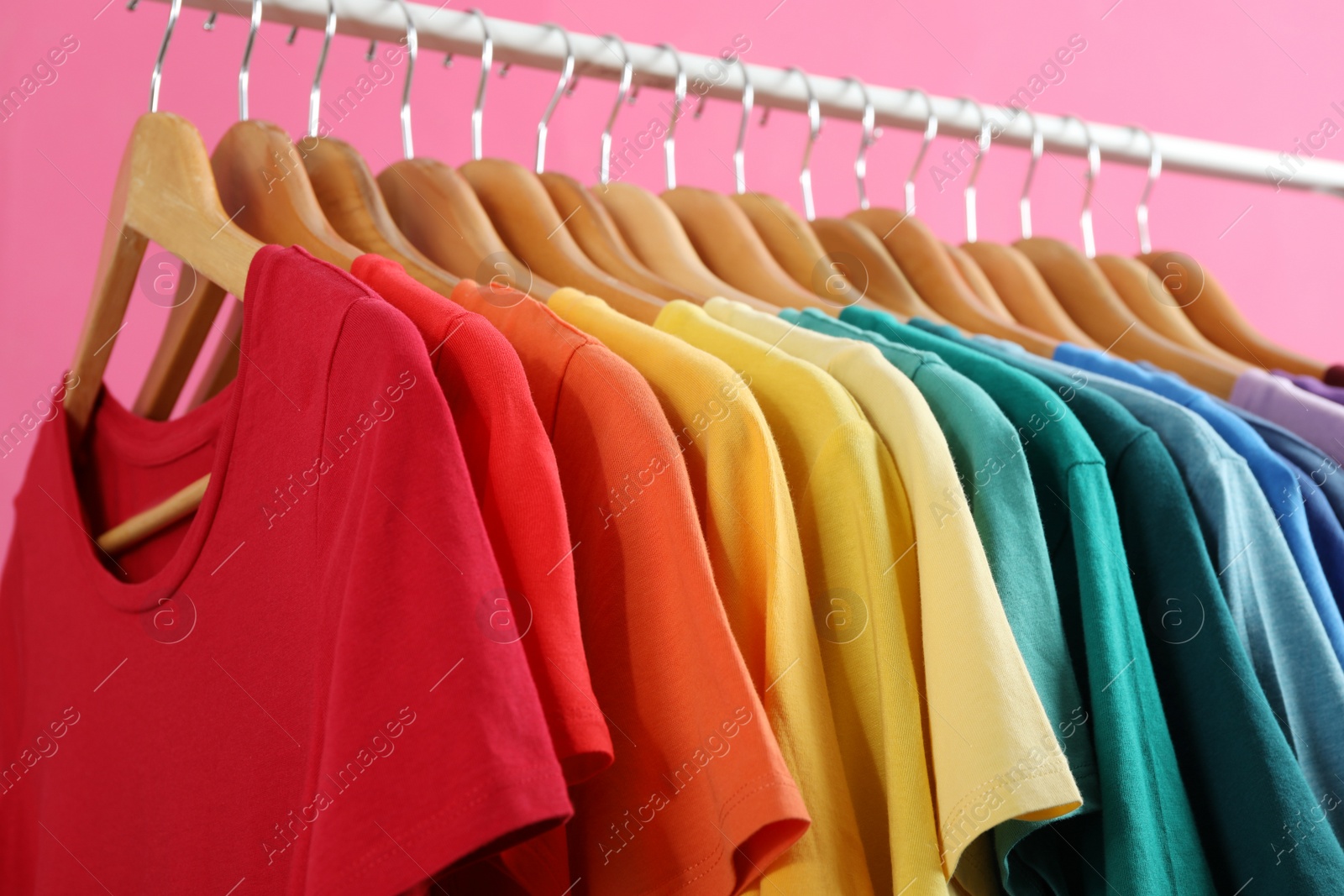 Photo of Rack with bright clothes on pink background, closeup