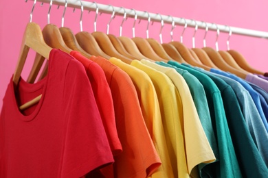 Rack with bright clothes on pink background, closeup