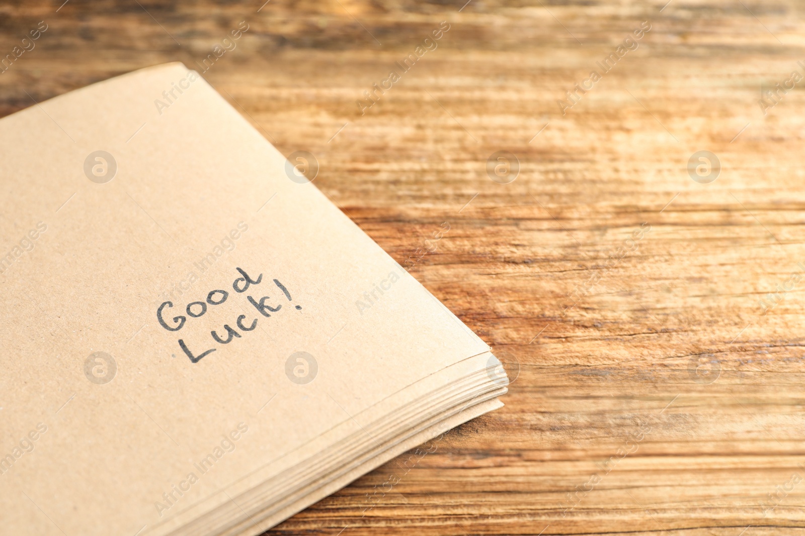 Photo of Notebook with phrase GOOD LUCK on wooden table, closeup. Space for text
