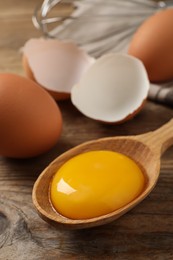 Raw chicken eggs and spoon with yolk on wooden table