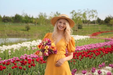 Happy woman with spring bouquet of flowers in beautiful tulip field on sunny day