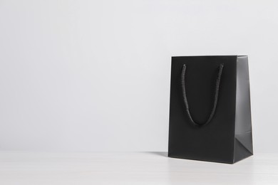 Black paper bag on white wooden table, space for text