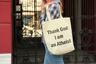 Woman holding bag with phrase Thank God I Am Atheist outdoors, closeup