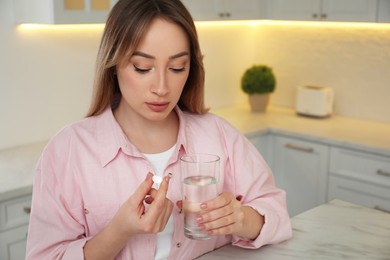 Young woman with abortion pill and water in kitchen