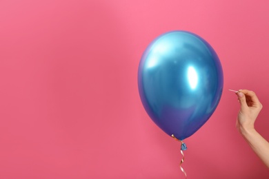 Photo of Woman piercing balloon with needle on color background, closeup. Space for text