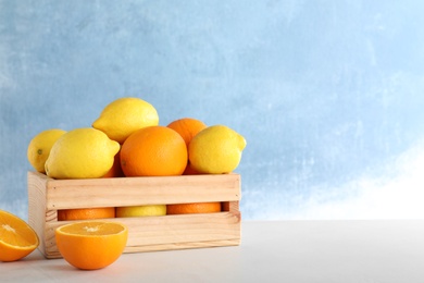 Photo of Wooden crate full of fresh juicy oranges and lemons on table against color background, space for text