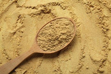 Photo of Heap of aromatic mustard powder and wooden spoon, top view