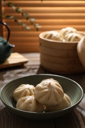 Photo of Delicious bao buns (baozi) in bowl on wooden table, closeup