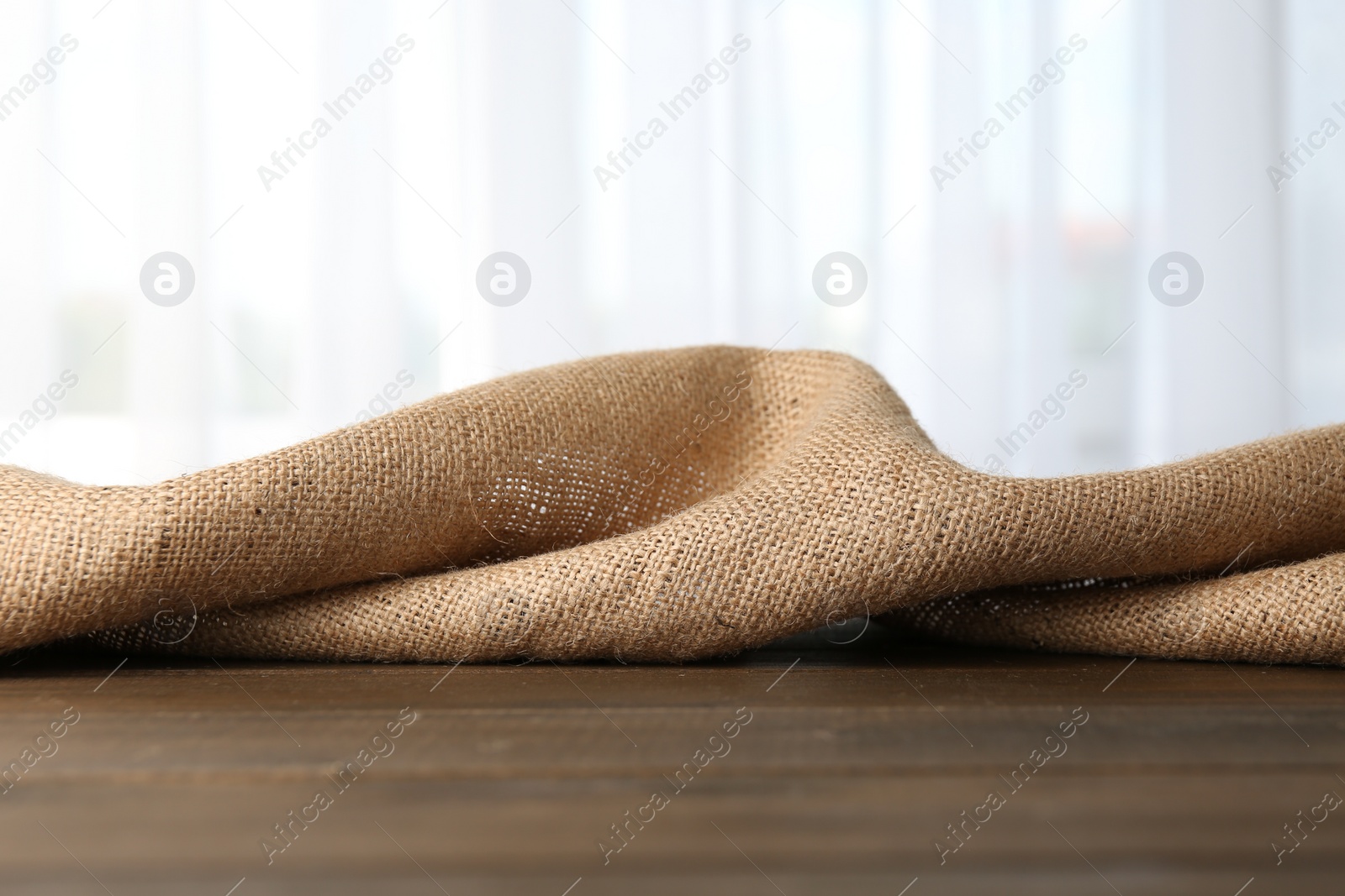 Photo of Brown burlap fabric on wooden table, closeup