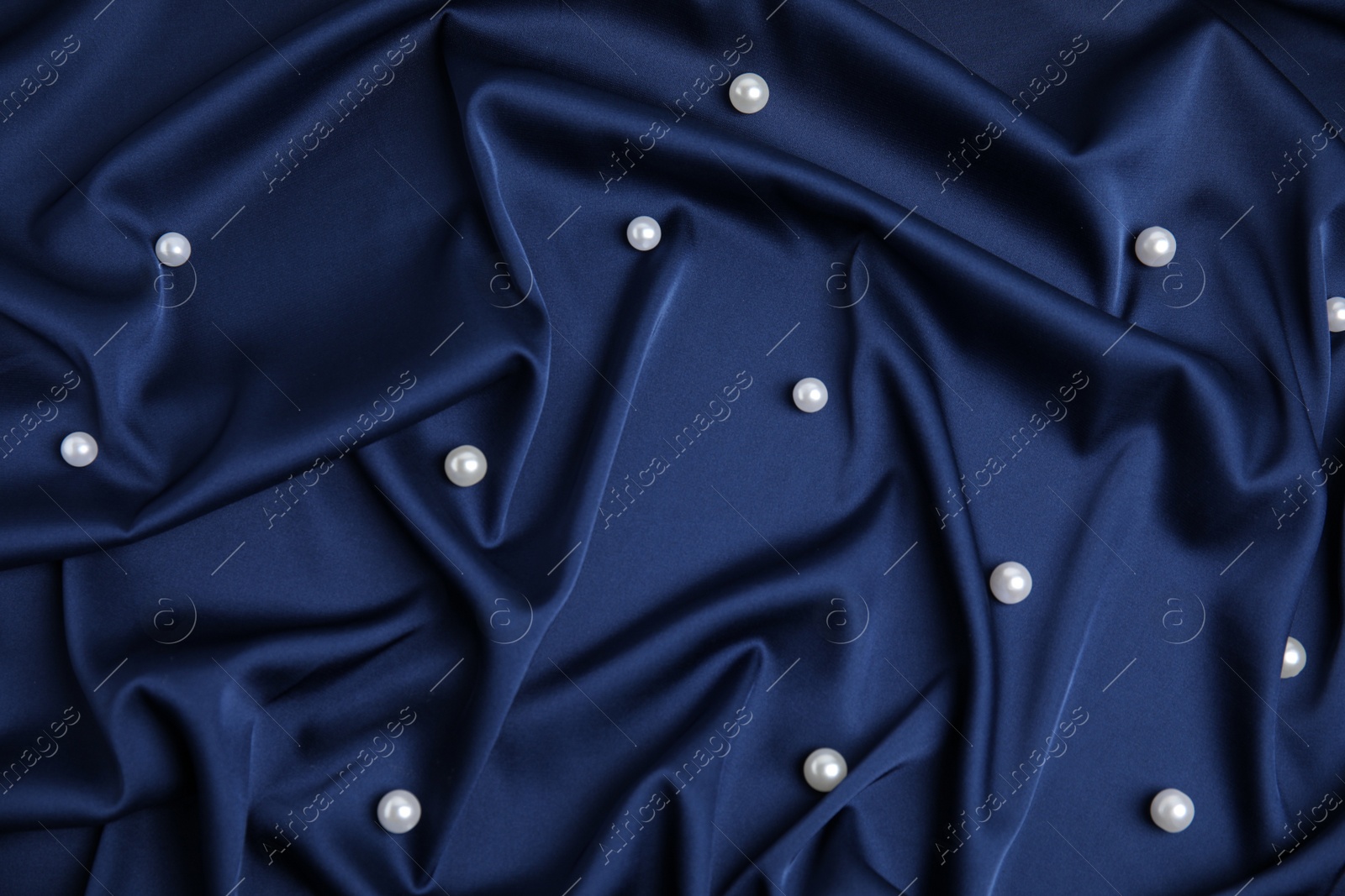 Photo of Many beautiful pearls on delicate dark blue silk, flat lay