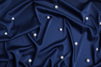 Photo of Many beautiful pearls on delicate dark blue silk, flat lay