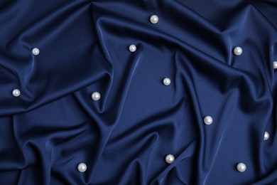 Many beautiful pearls on delicate dark blue silk, flat lay