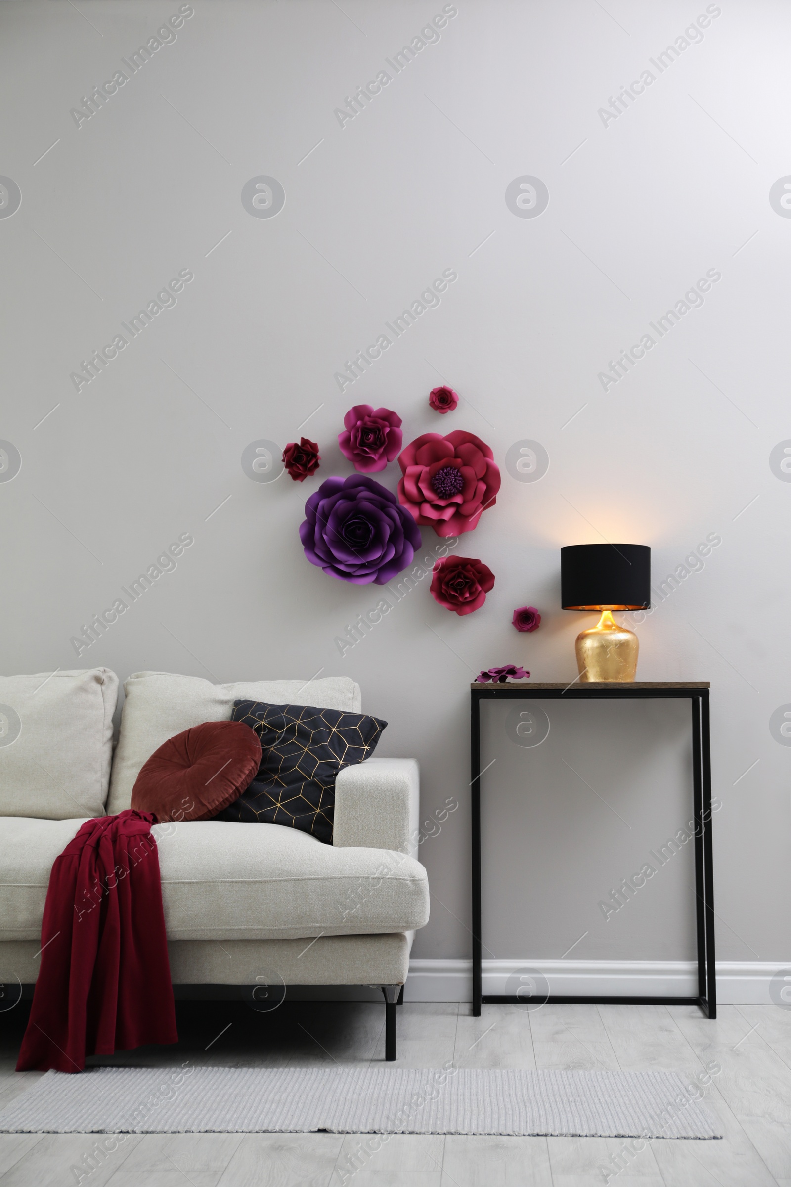 Photo of Comfortable sofa and table near wall with floral decor in living room