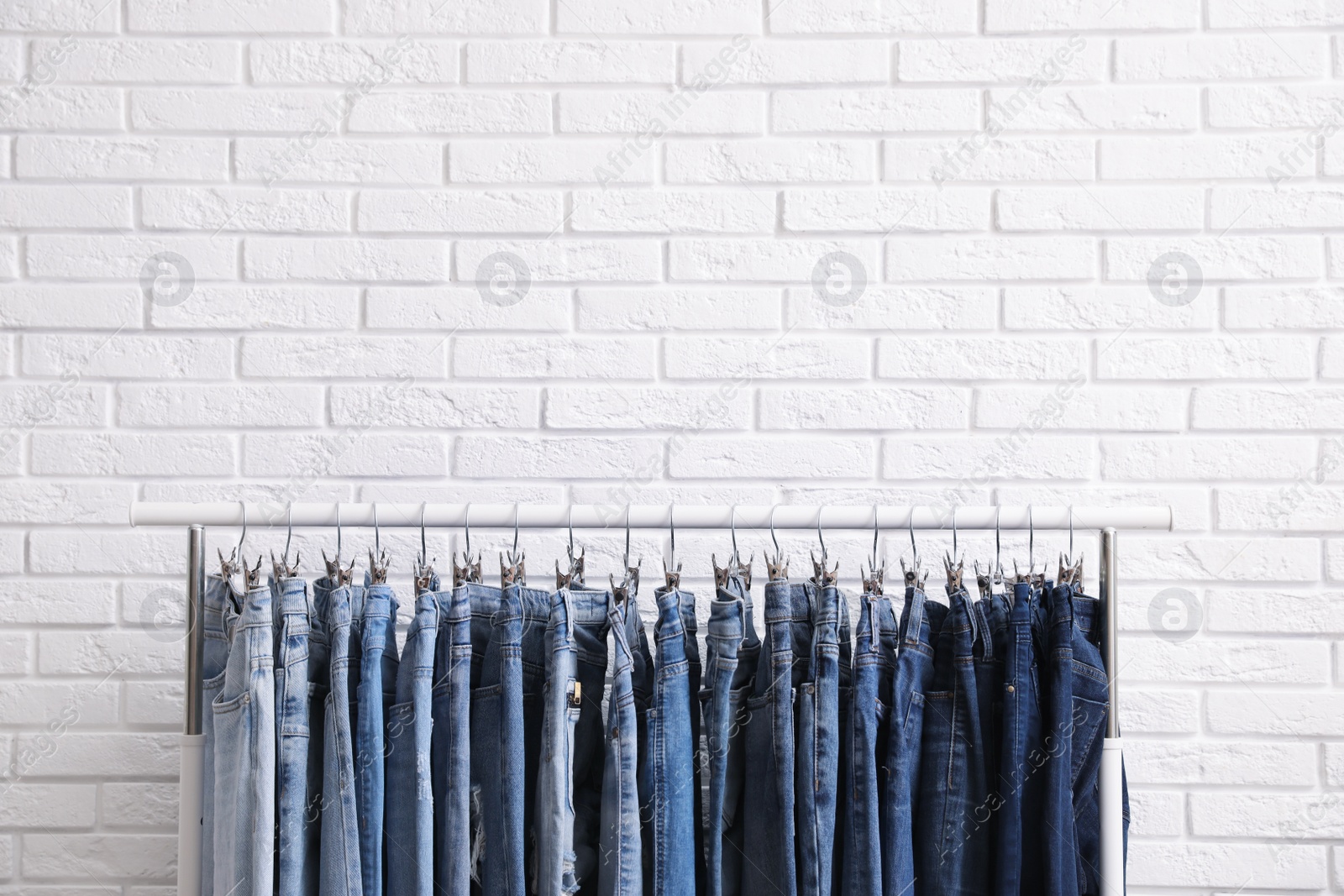 Photo of Rack with stylish jeans near brick wall. Space for text