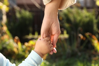 Daughter holding mother's hand outdoors, closeup view