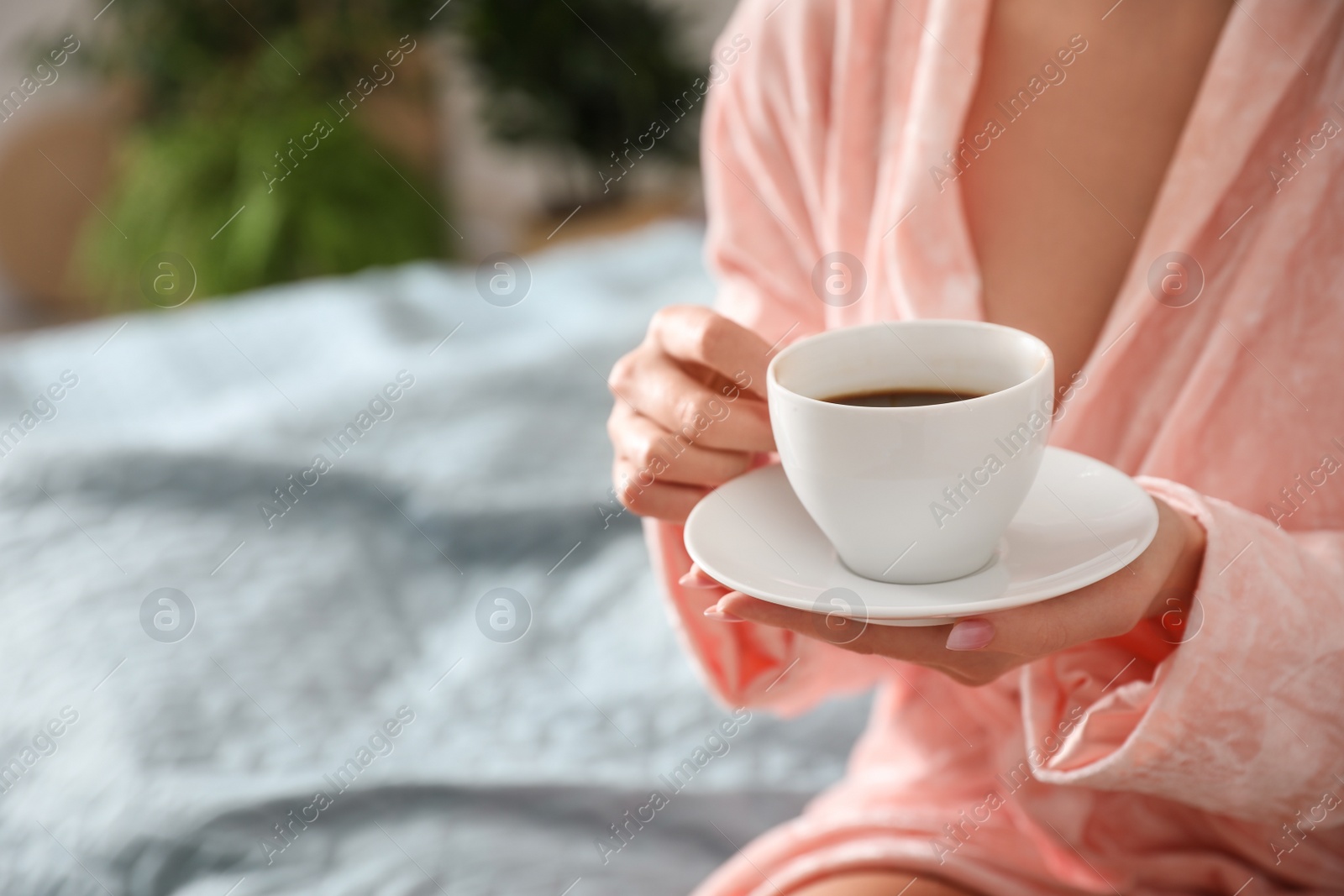 Photo of Woman with cup of hot coffee and blurred plants on background, closeup. Home decor