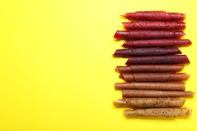 Photo of Delicious fruit leather rolls on yellow background, flat lay. Space for text