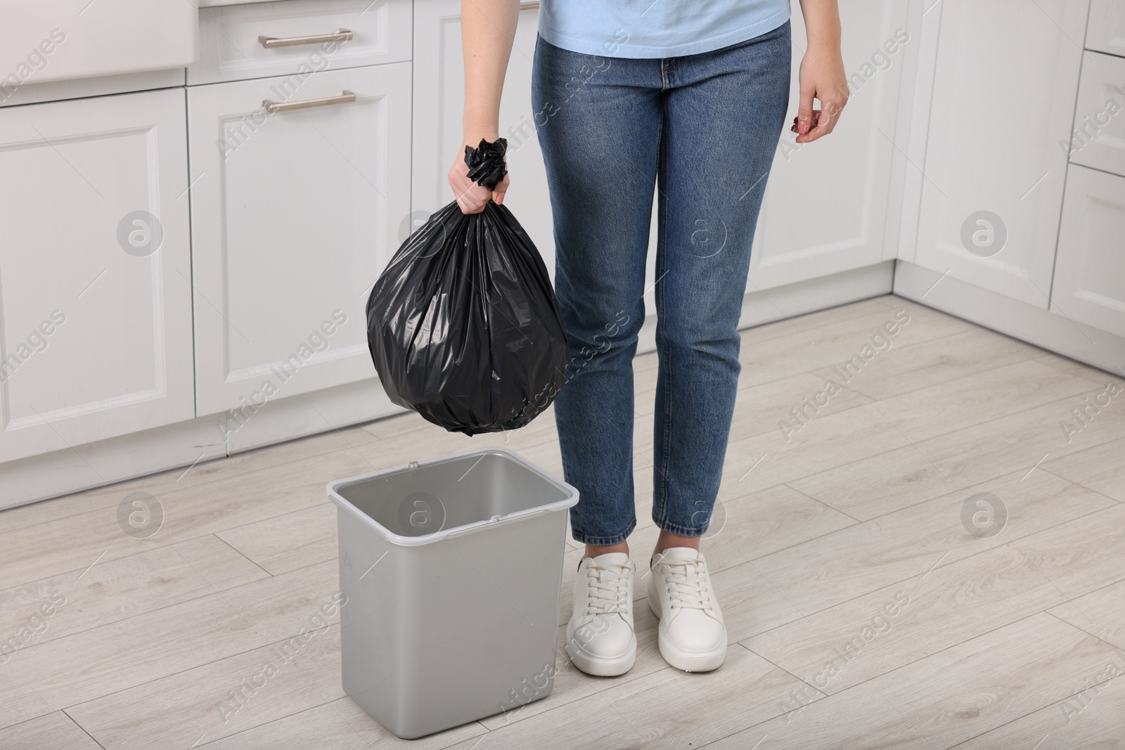 Photo of Woman taking garbage bag out of trash bin in kitchen, closeup