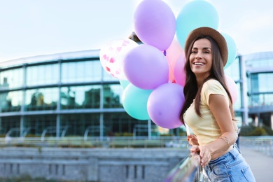 Beautiful young woman with color balloons on city street