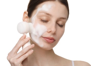 Young woman washing face with brush and cleansing foam on white background