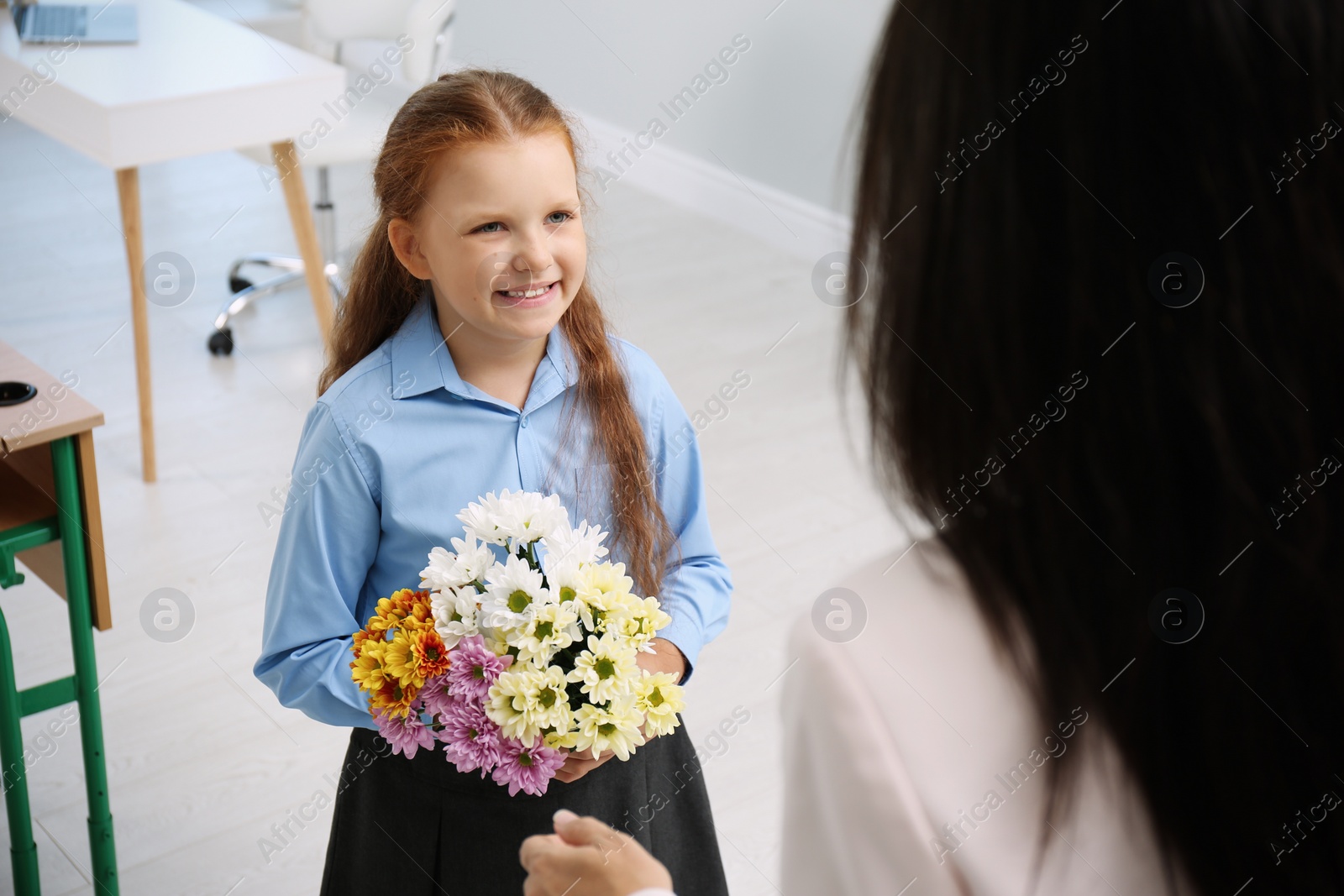 Photo of Schoolgirl with bouquet congratulating her pedagogue in classroom. Teacher's day