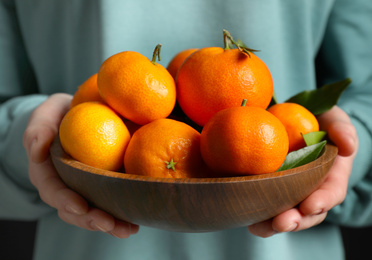 Photo of Woman holding bowl of tangerines, closeup. Juicy citrus fruit